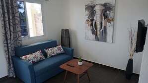 Un salon avec un canapé bleu, une petite table basse en bois, une télécommande et un cactus.