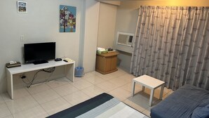 A compact room with a bed, a desk with a TV, a small table, a curtain, and a wall-mounted air conditioner. - Tainan Here Hostel 2 (Tainan)