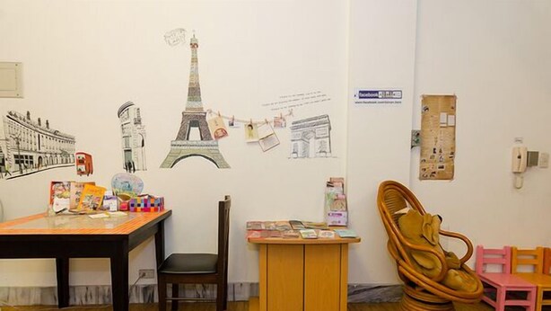 A room with a wooden table, a chair, a small wooden cabinet, and a wall decorated with illustrations of famous landmarks. - Tainan Here Hostel 2 (Tainan)
