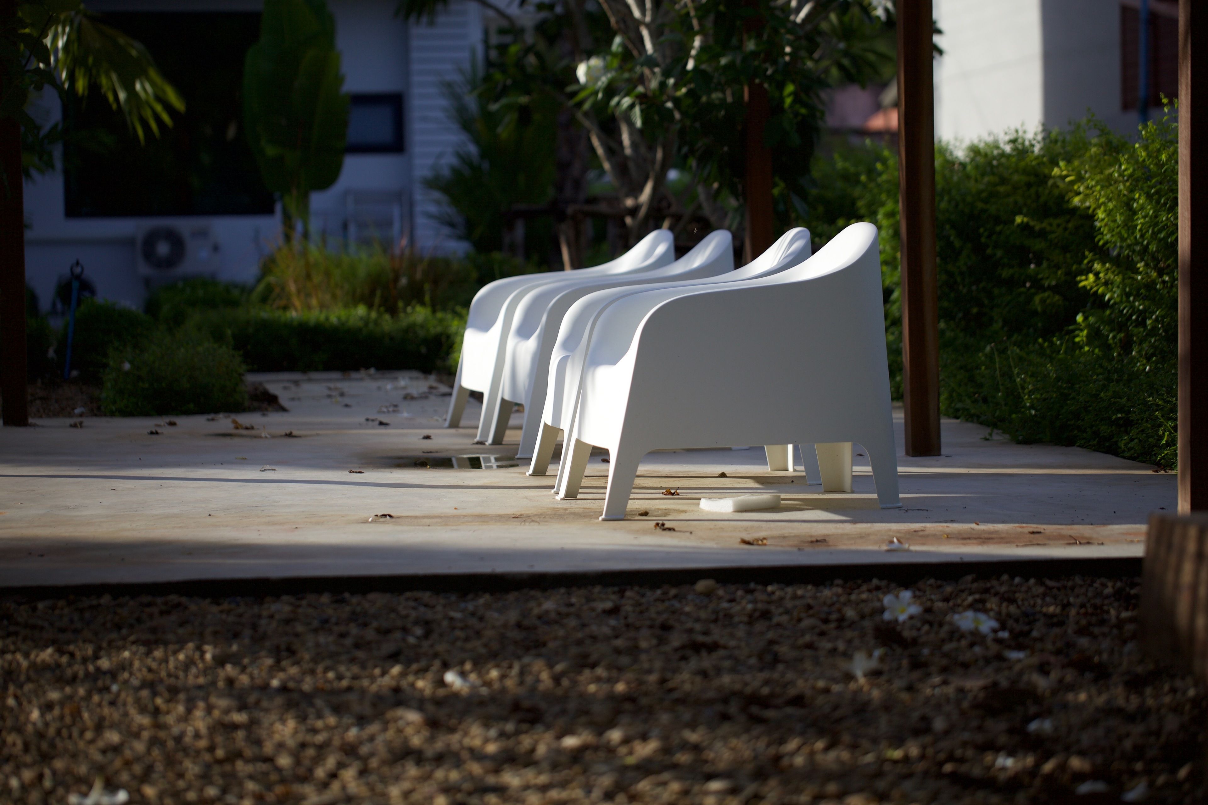 A row of white benches with a concrete pathway and greenery in the background.