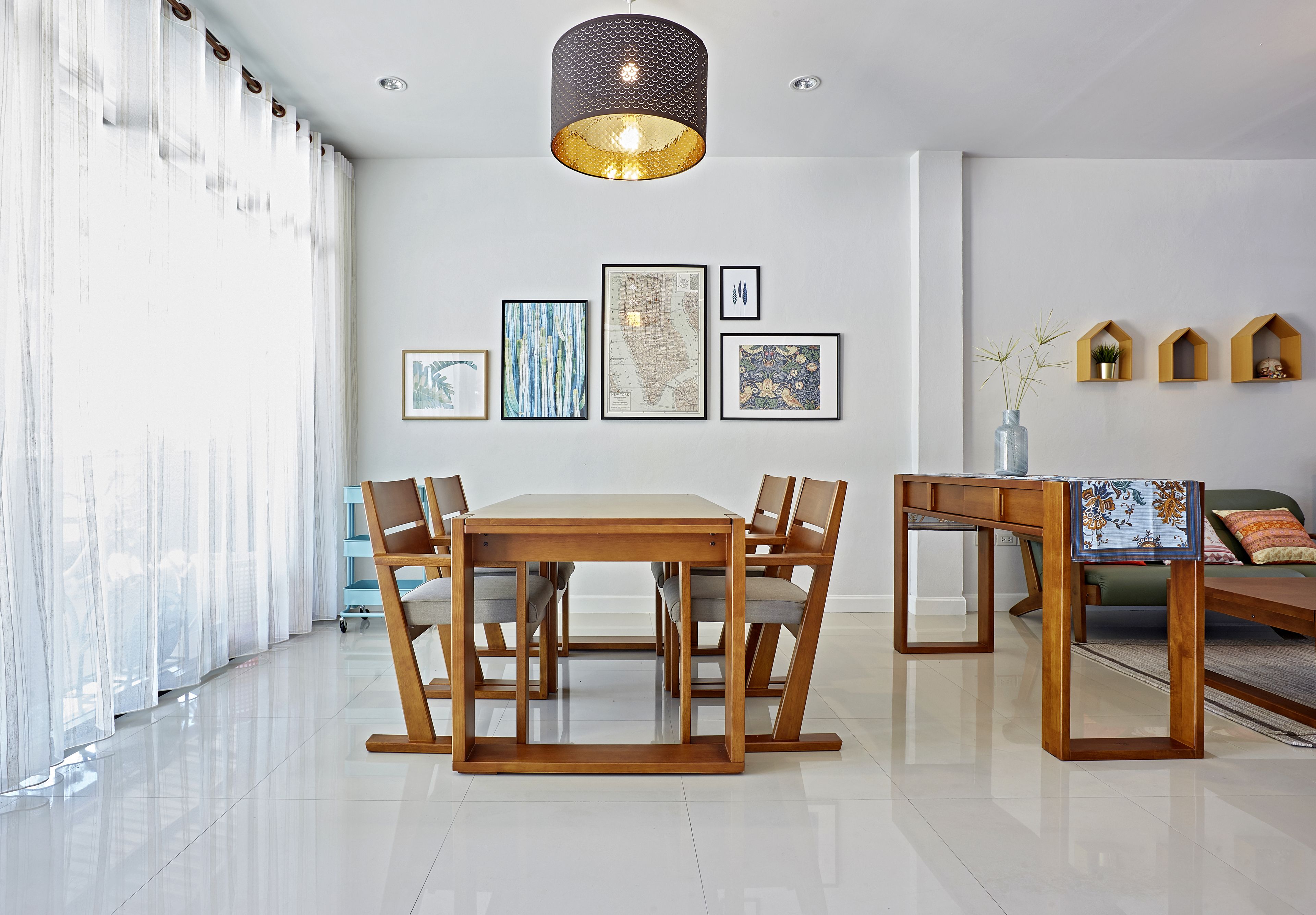 A modern dining area with a wooden table and chairs, a hanging pendant light, and framed artwork on the wall.