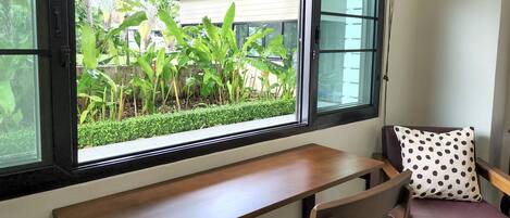 Una habitación con escritorio y silla, una ventana con vista a follaje, y un cojín de lunares.