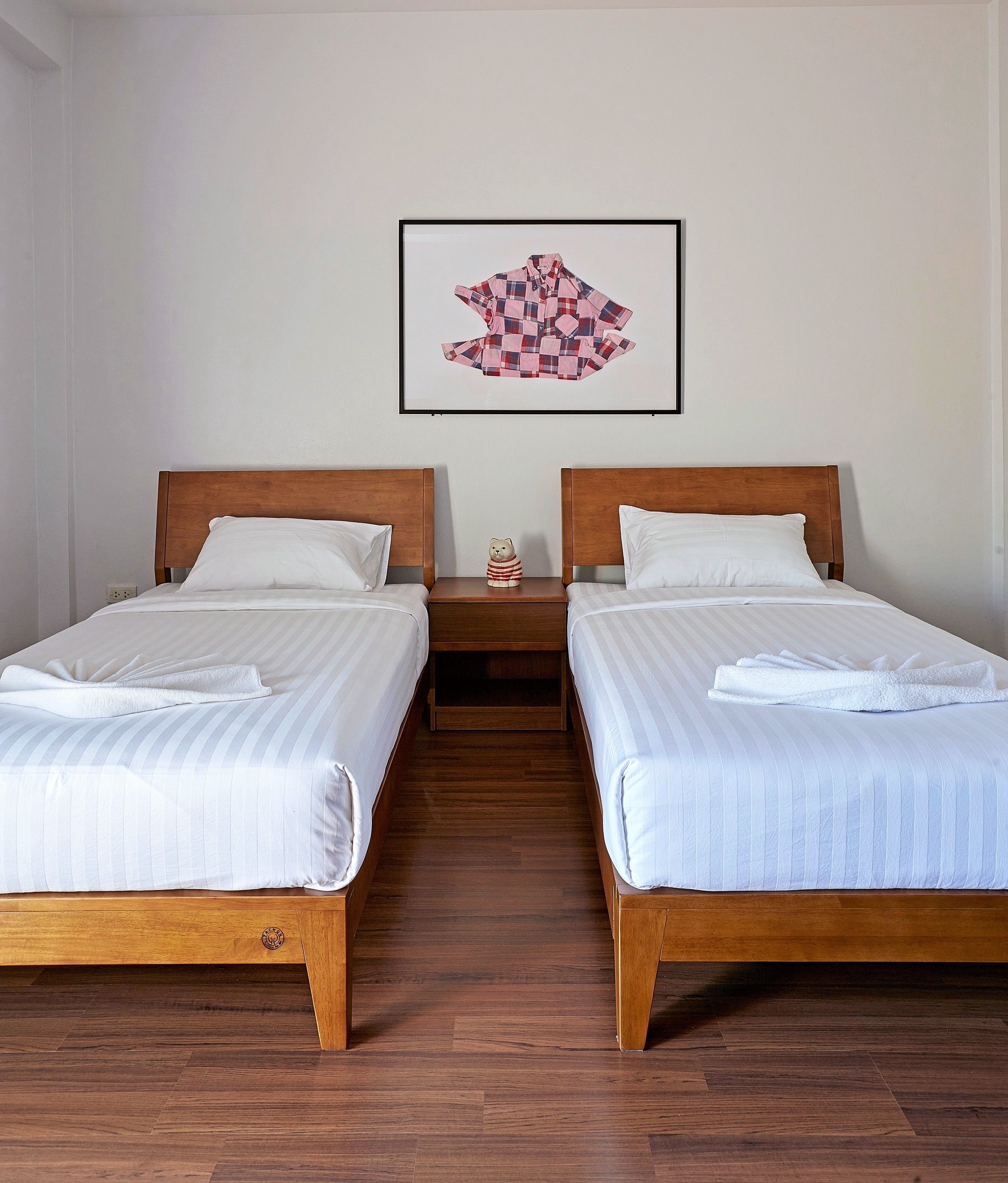 Habitación de hotel con dos camas individuales, cabeceras de madera, ropa de cama blanca, una mesita de noche con un oso de peluche y una obra de arte enmarcada en la pared.