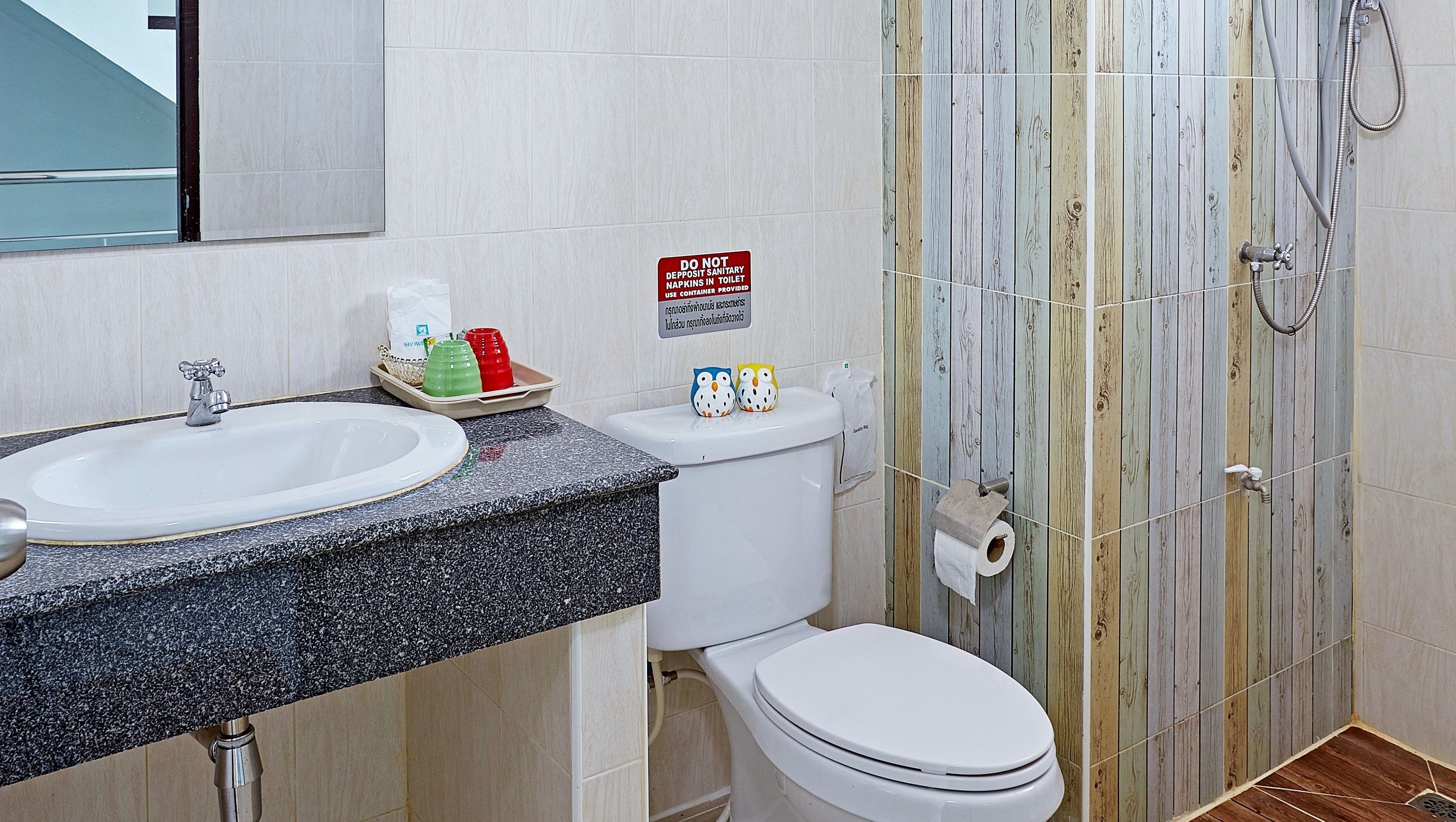 A bathroom with a sink, toilet, and shower. There is a sign instructing not to deposit sanitary napkins in the toilet.