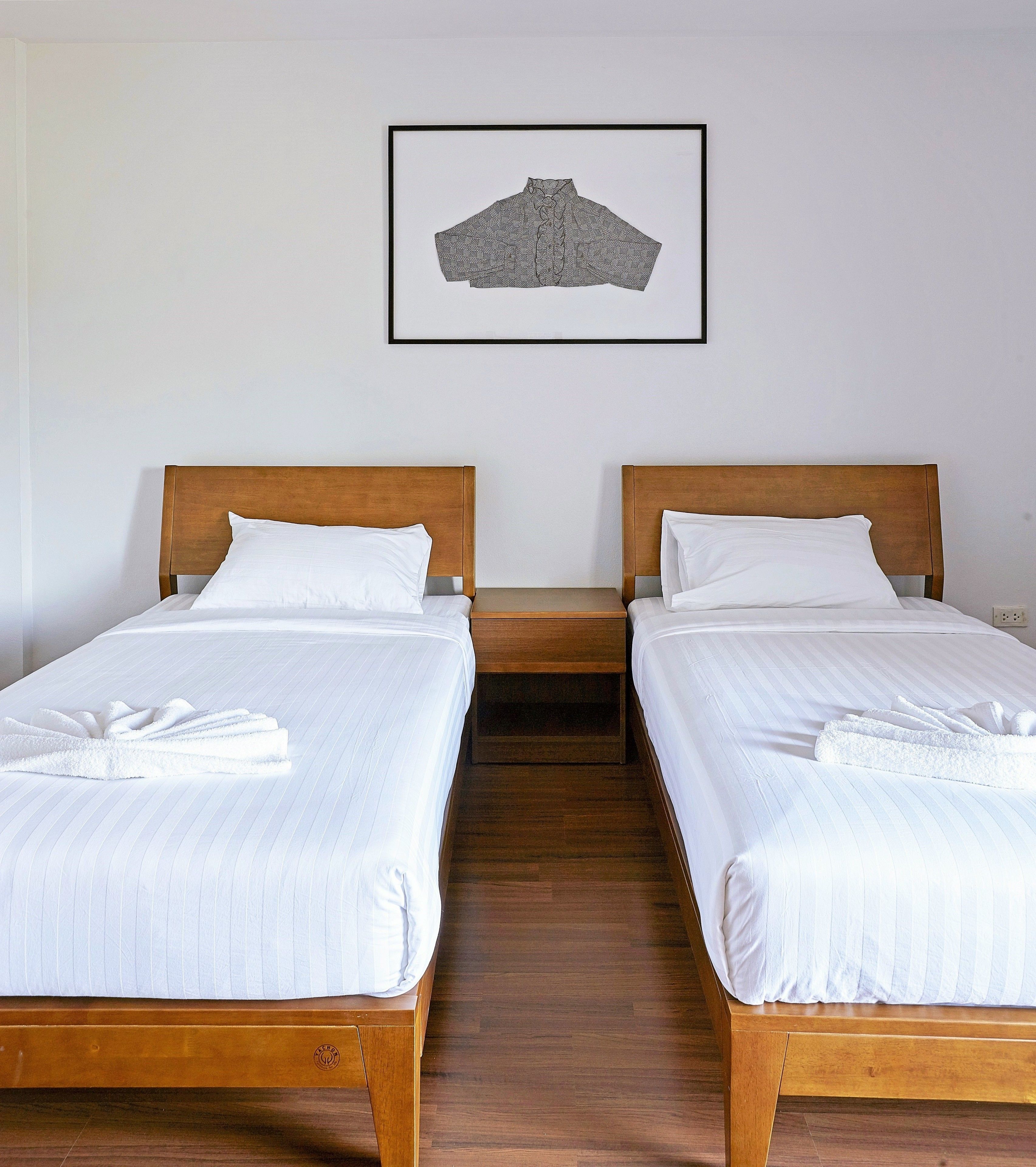 Two single beds with wooden headboards and white linens, a framed picture on the wall, and a wooden floor.