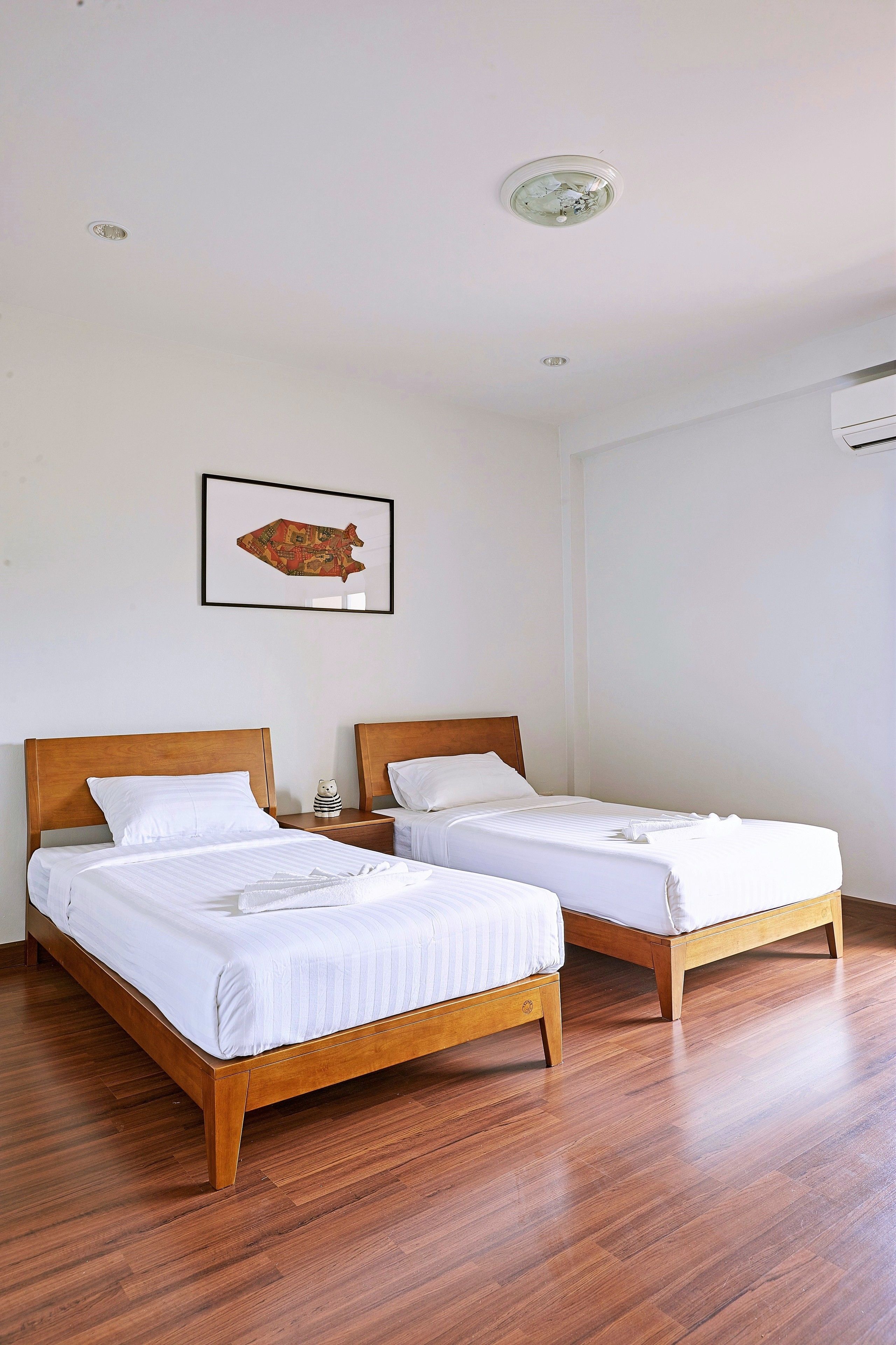 A hotel room with two wooden beds, white bedding, a framed fish artwork on the wall, and a ceiling light fixture.