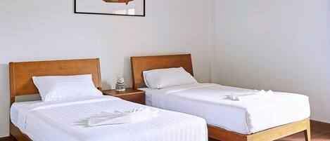 A hotel room with two wooden beds, white bedding, a framed fish artwork on the wall, and a ceiling light fixture.