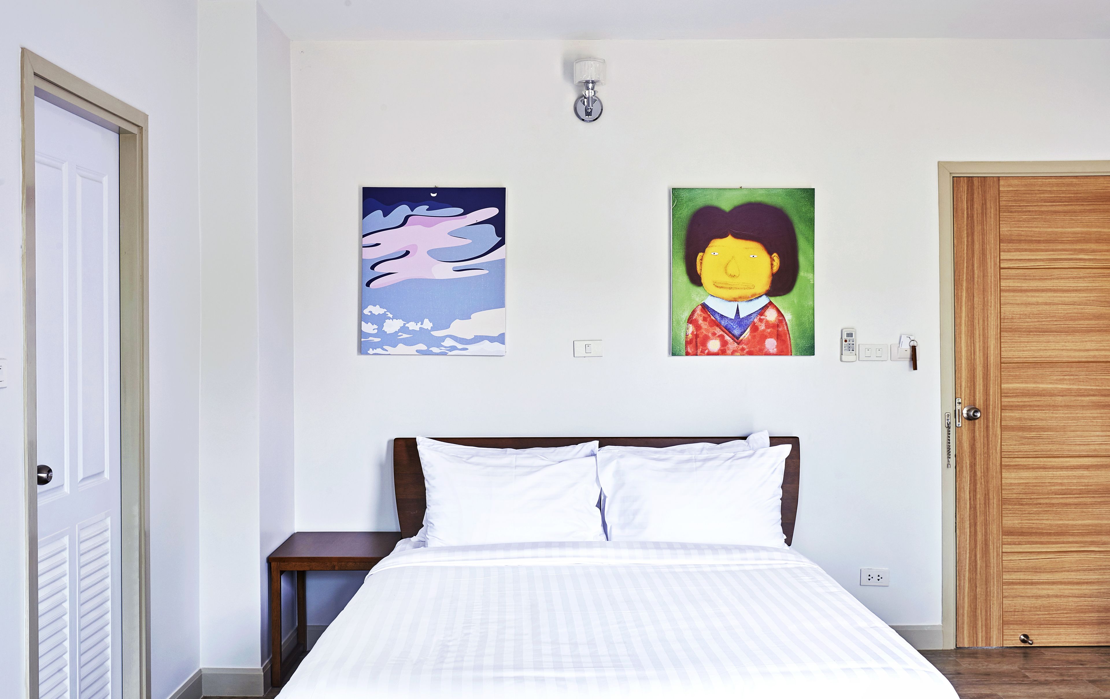 A bedroom with a bed, a nightstand, a wall-mounted light, and two paintings.