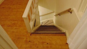A wooden staircase with white railings and a handrail, leading to an upper floor. - Just You Vacation Home (Gilbert Plains)