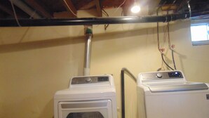 A laundry room with two stacked washers and dryers, a visible ductwork, and a window with a view. - Just You Vacation Home (Gilbert Plains)