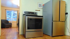 A kitchen with a stainless steel oven and refrigerator, wooden flooring, a window with a view of trees, and a framed picture on the wall. - Just You Vacation Home (Gilbert Plains)
