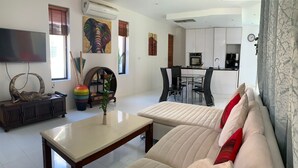 A modern living room with a sofa, a coffee table, a TV, and a dining area with a kitchen in the background. - 3 Bedroom Villa SDV261- Walk to Beach-By Samui Dream Villas (Koh Samui)