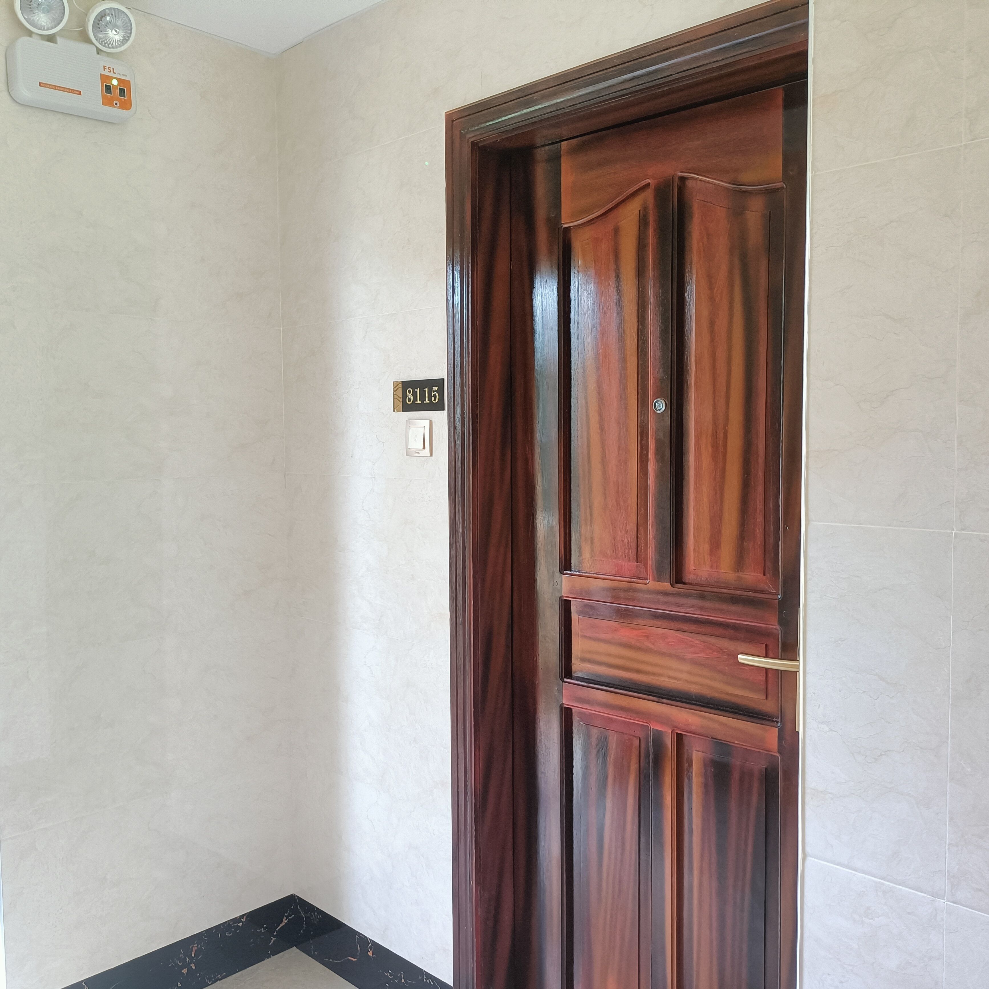 A wooden door with a number plate, a light switch, and a power outlet on the wall.