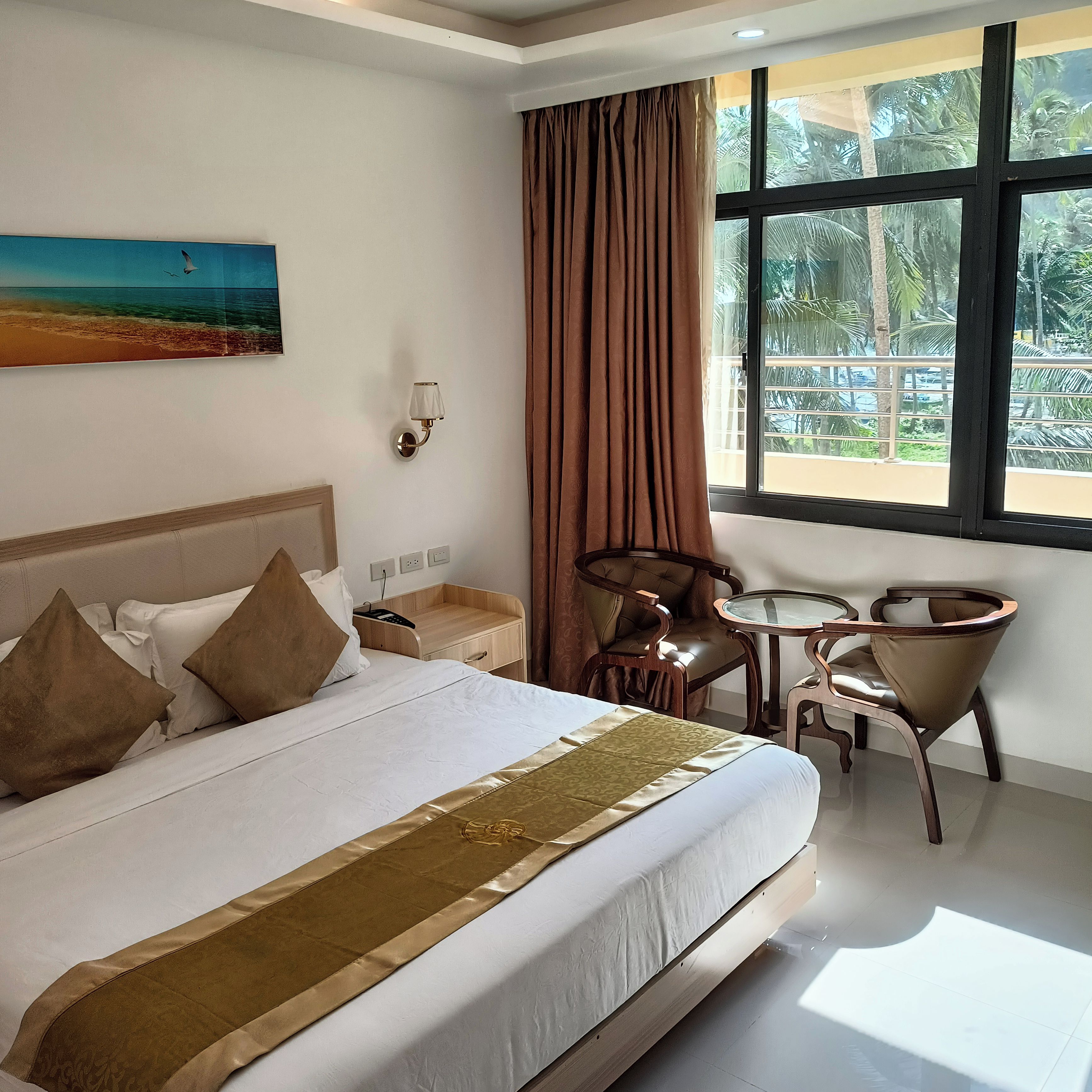 A hotel room with a bed, a desk, a chair, a window with curtains, and a painting on the wall.