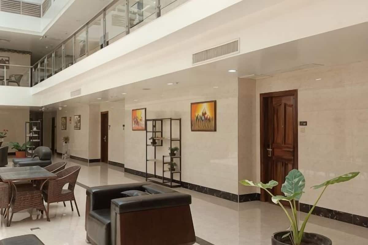 Um hall amplo com teto alto, área de estar com mesas e cadeiras, balcão de recepção e escada que dá acesso a um andar superior.