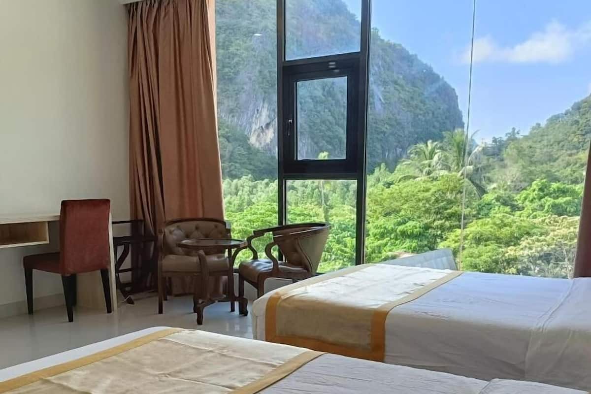 Quarto de hotel com duas camas, uma escrivaninha, uma cadeira e vista para uma paisagem verde exuberante.