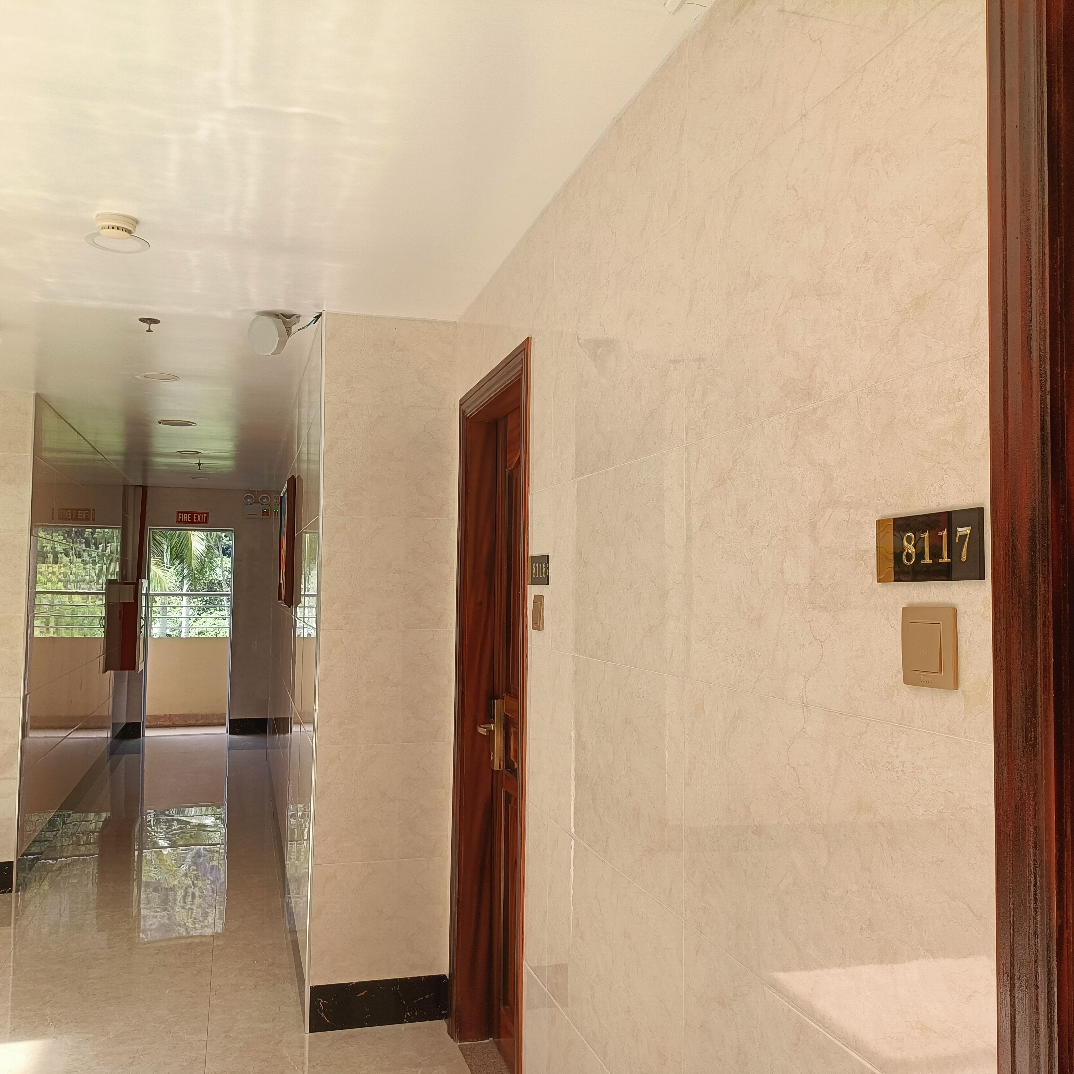 A hallway with a polished floor, a wooden door, and a number plate indicating room 8117.
