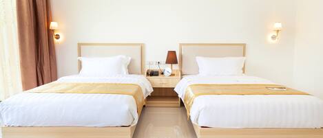 Hotellihuone, jossa on kaksi sänkyä, yöpöytä lampun kanssa ja seinälle asennettu puhelin.