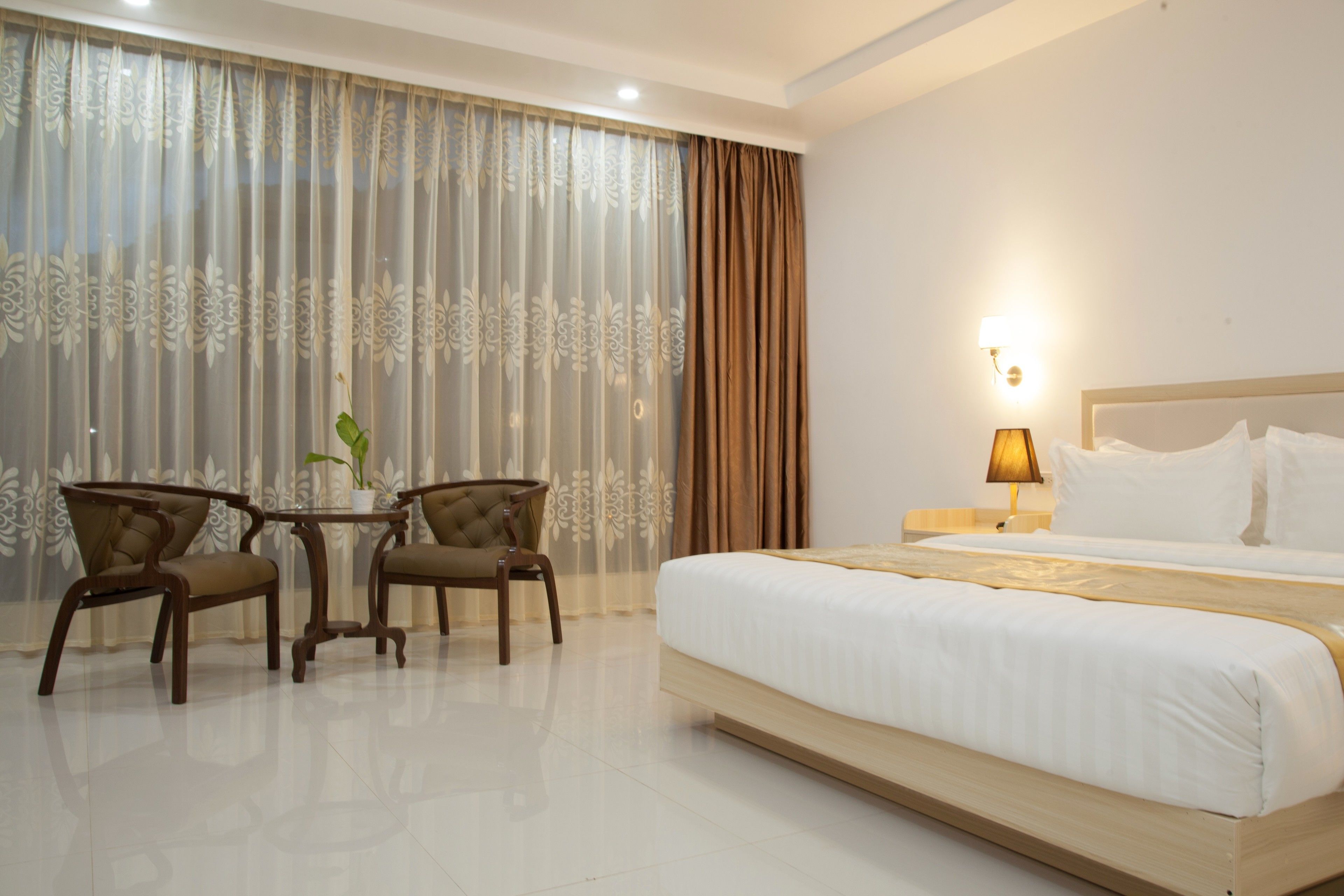 A hotel room with a bed, two chairs, a small table with a plant, and a lamp.