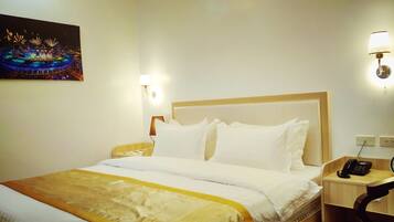 Quarto de hotel com uma cama grande, mesa de cabeceira com abajur, telefone e um quadro na parede.