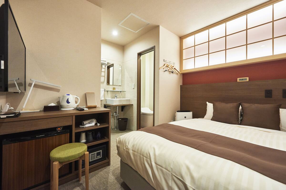 A hotel room with a bed, a desk with a computer, a chair, a sink, and a mirror.