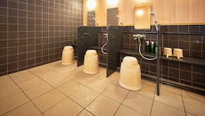 Des toilettes publiques équipées de trois lavabos, avec des murs recouverts de carreaux noirs et un lambris en bois.