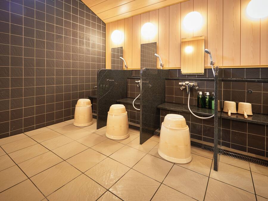 A public restroom with three sinks, black tiled walls, and wooden paneling.