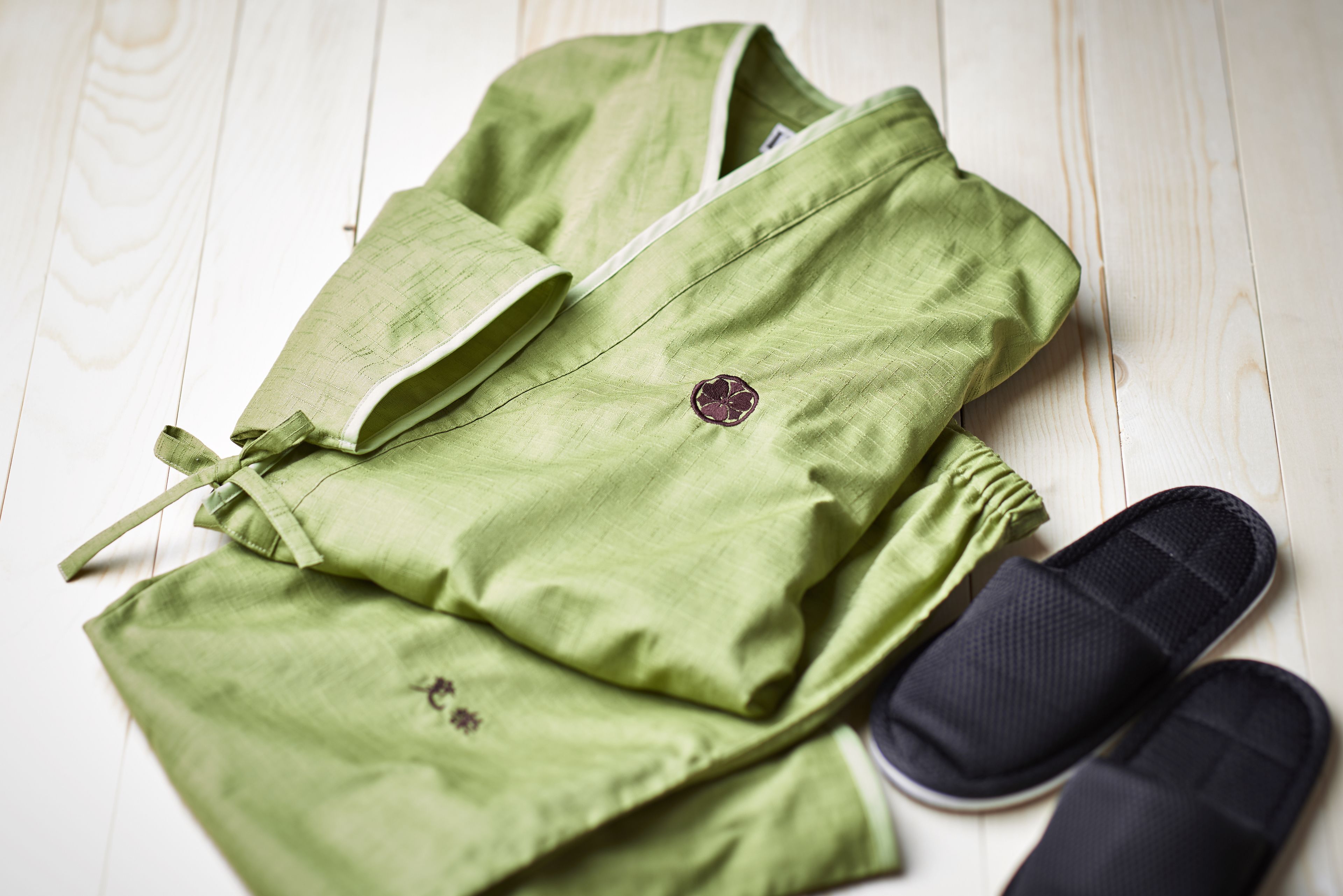 A pair of green pants and black slippers on a wooden floor.