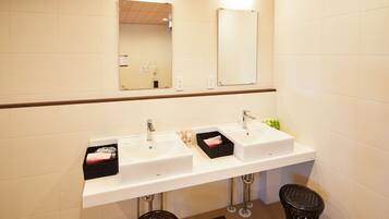 A modern bathroom with two sinks, a mirror, and a trash bin.