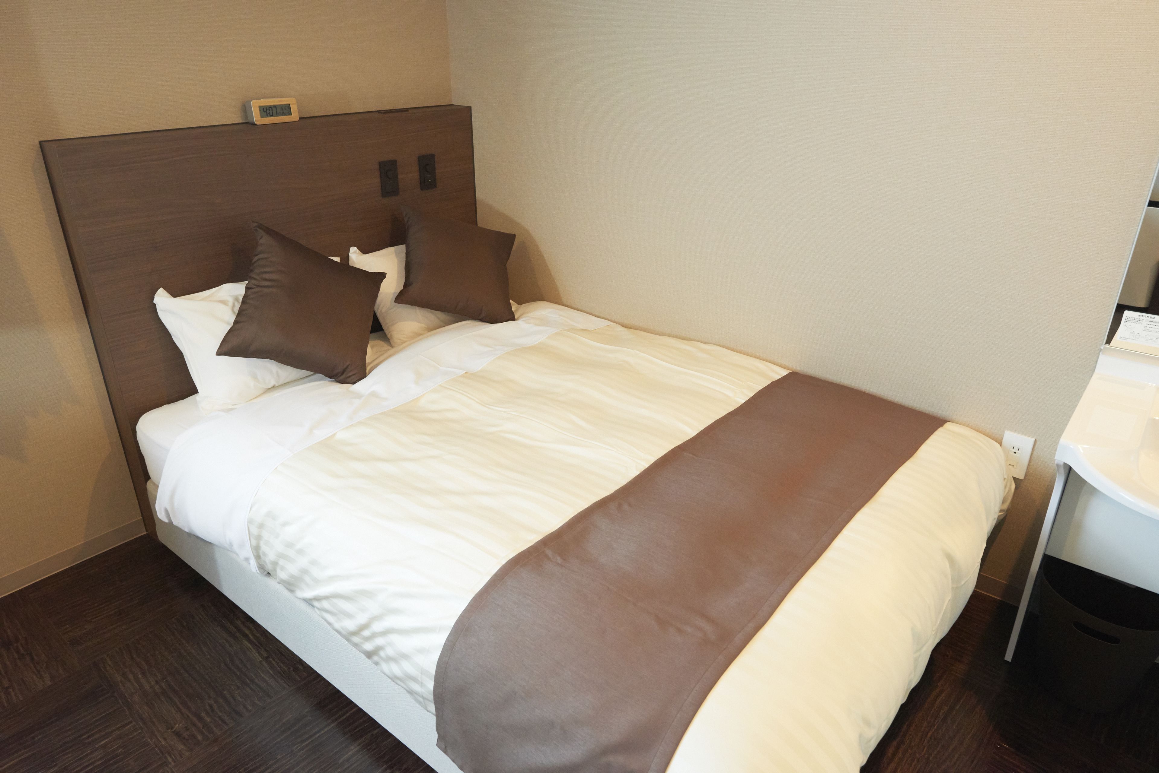 Een keurig opgemaakt bed met een bruin hoofdeinde, wit beddengoed en twee bruine kussens.