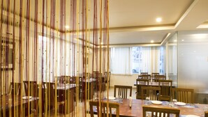 A dining area with multiple tables and chairs, a large window with curtains, and a decorative hanging element. - Rainbow International Shamshabad (Hyderabad)