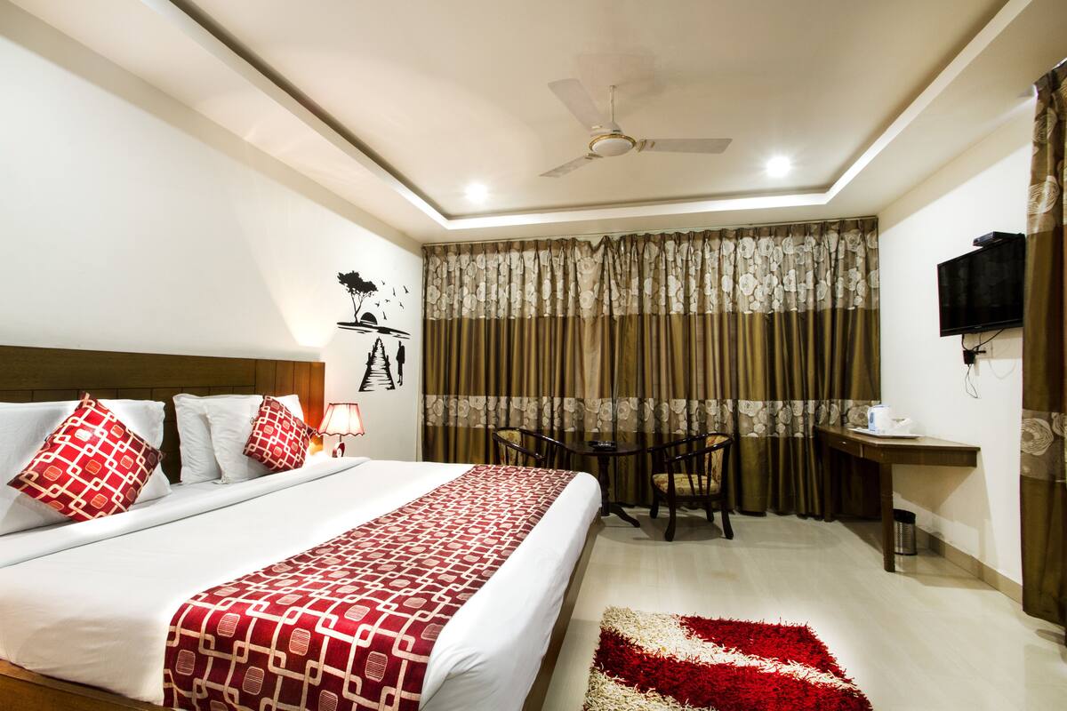 Habitación de hotel con cama, escritorio, silla, ventilador de techo y televisor.