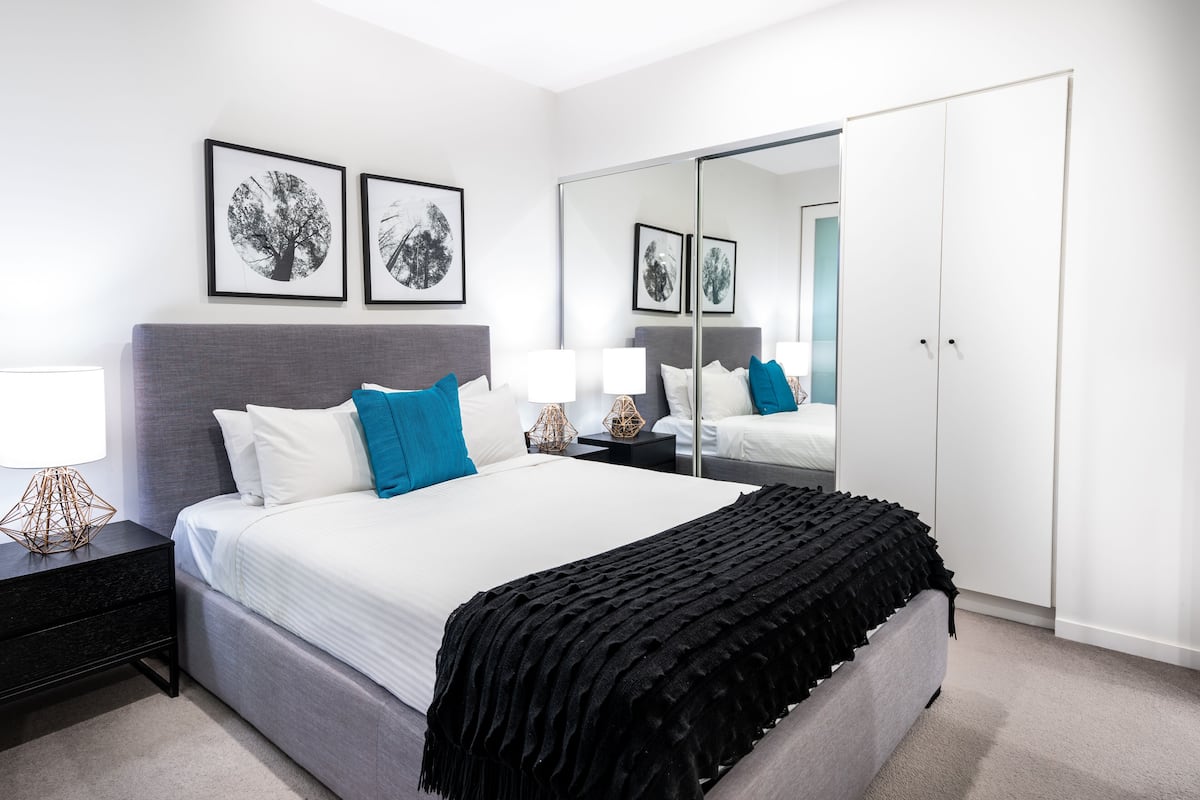 Un dormitorio moderno con una cama grande, una mesita de noche, un aparador y un espejo.