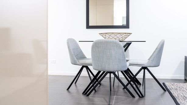 A modern dining area with a minimalist design, featuring a table with a geometric metal centerpiece, two grey upholstered chairs with black legs, and a large mirror on the wall. - Opera Apartments South Brisbane (South Brisbane)