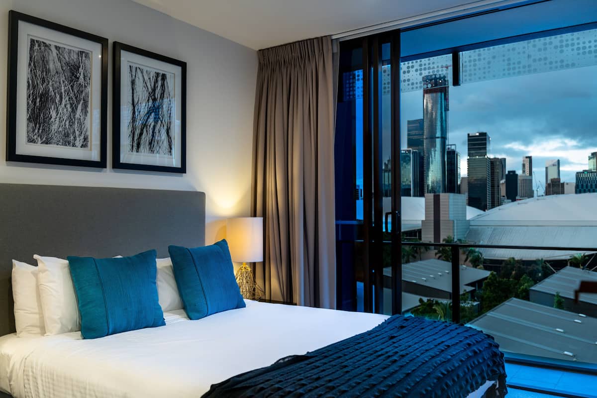 Habitación de hotel con una cama grande, vistas a la ciudad y dos cuadros enmarcados en la pared.