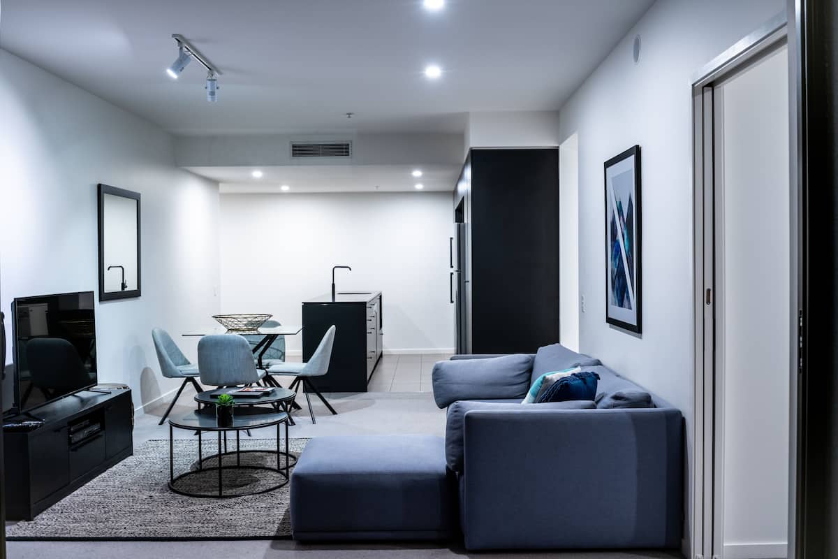Una sala de estar moderna con un sofá gris, una mesa de centro, un televisor y un comedor con sillas y una mesa.
