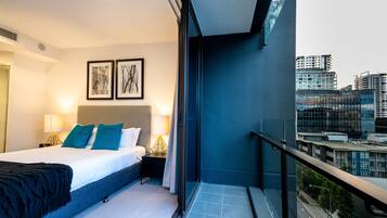 A modern hotel room with a large bed, a nightstand, a lamp, and two framed artworks on the wall.