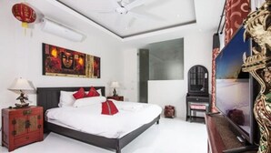 Una camera da letto con un letto, due comodini, un tavolino, una ventola a soffitto, una TV a muro e uno specchio decorativo.