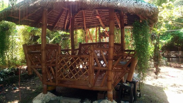 A bamboo structure with a thatched roof, surrounded by lush greenery. - Emok's Guest House - Hostel (Moalboal)