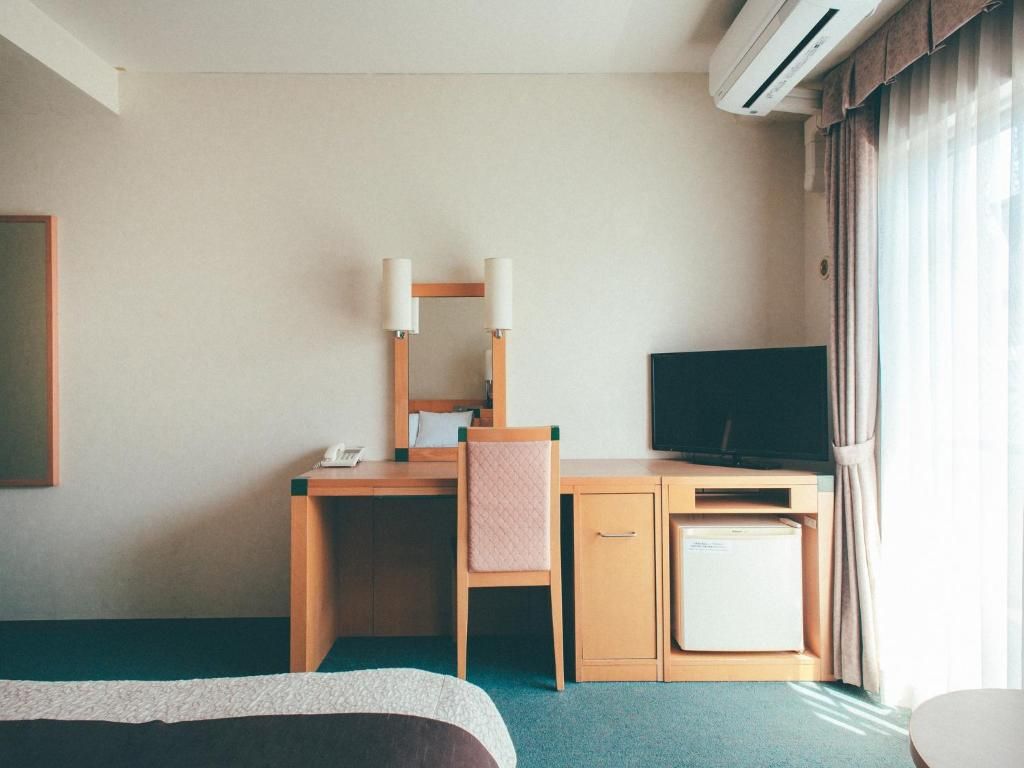 A hotel room with a bed, a desk with a chair, a television, and a mini-fridge.