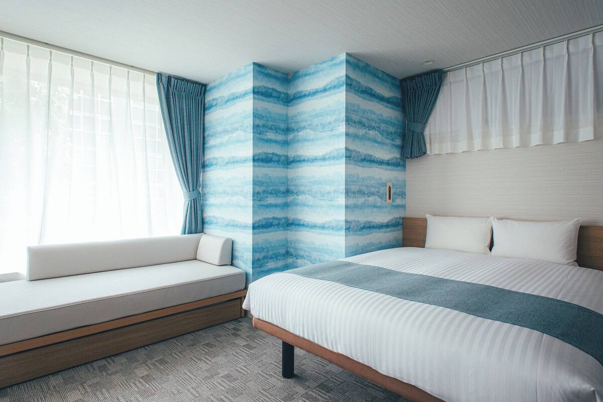 A hotel room with a bed, a sofa, and a large window with curtains.
