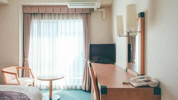 A hotel room with a bed, a desk with a telephone, a television, and a window with curtains.