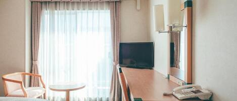 A hotel room with a bed, a desk with a telephone, a television, and a window with curtains.