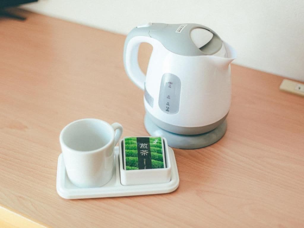 A white electric kettle with a digital display and a cup on a coaster with a green tea label.