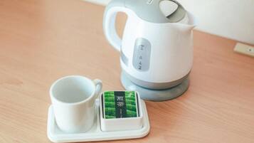 A white electric kettle with a digital display and a cup on a coaster with a green tea label.