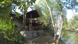 Une structure rustique en bois, dotée d’un mur en pierre, d’une terrasse en bois et d’un étang.