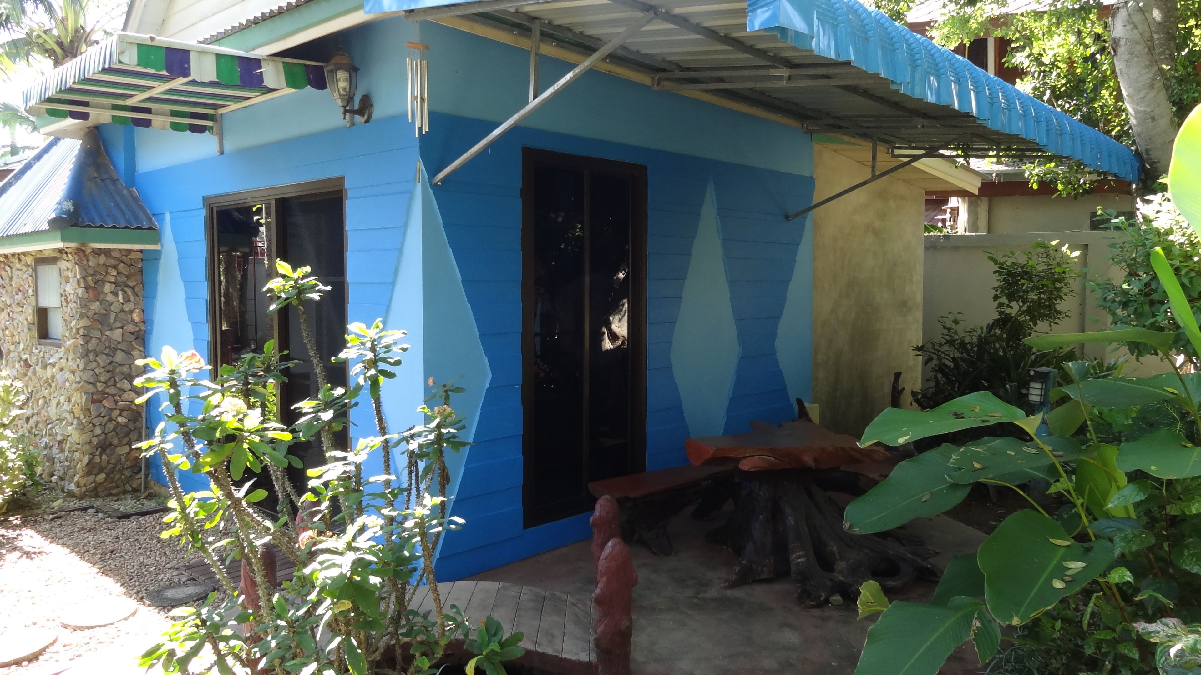 Una casa con fachada azul y blanca, un muro de piedra y un banco de madera.