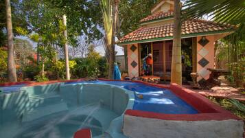 A swimming pool with a tiled deck, surrounded by lush greenery and a small pavilion.