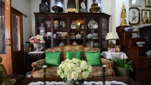 A traditional living room with a sofa, green cushions, a vase of flowers, and a cabinet filled with decorative items. - Villa 91 Guesthouse (Bangkok)