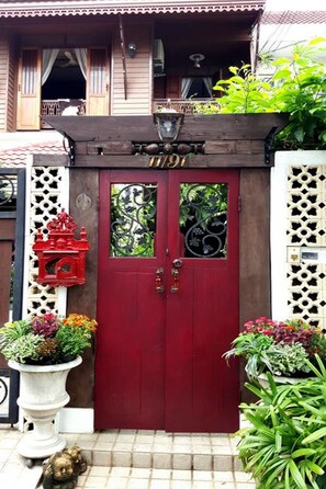 A red door with decorative glass panels, a small red lantern, and potted plants on either side. - Villa 91 Guesthouse (Bangkok)